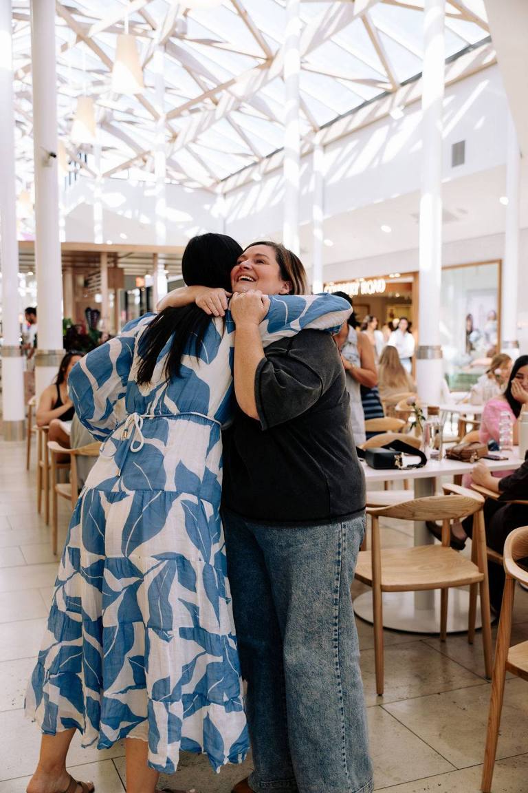 Two women in a big joyful hug at a Wanna Grab a Coffee morning in an Adelaide cafe