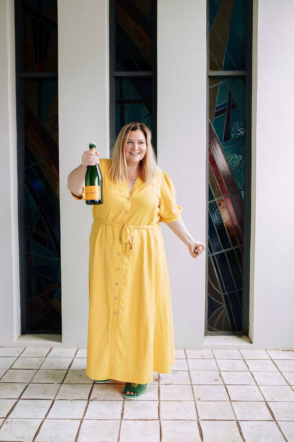 Woman in a yellow dress holding a bottle of champagne, celebrating