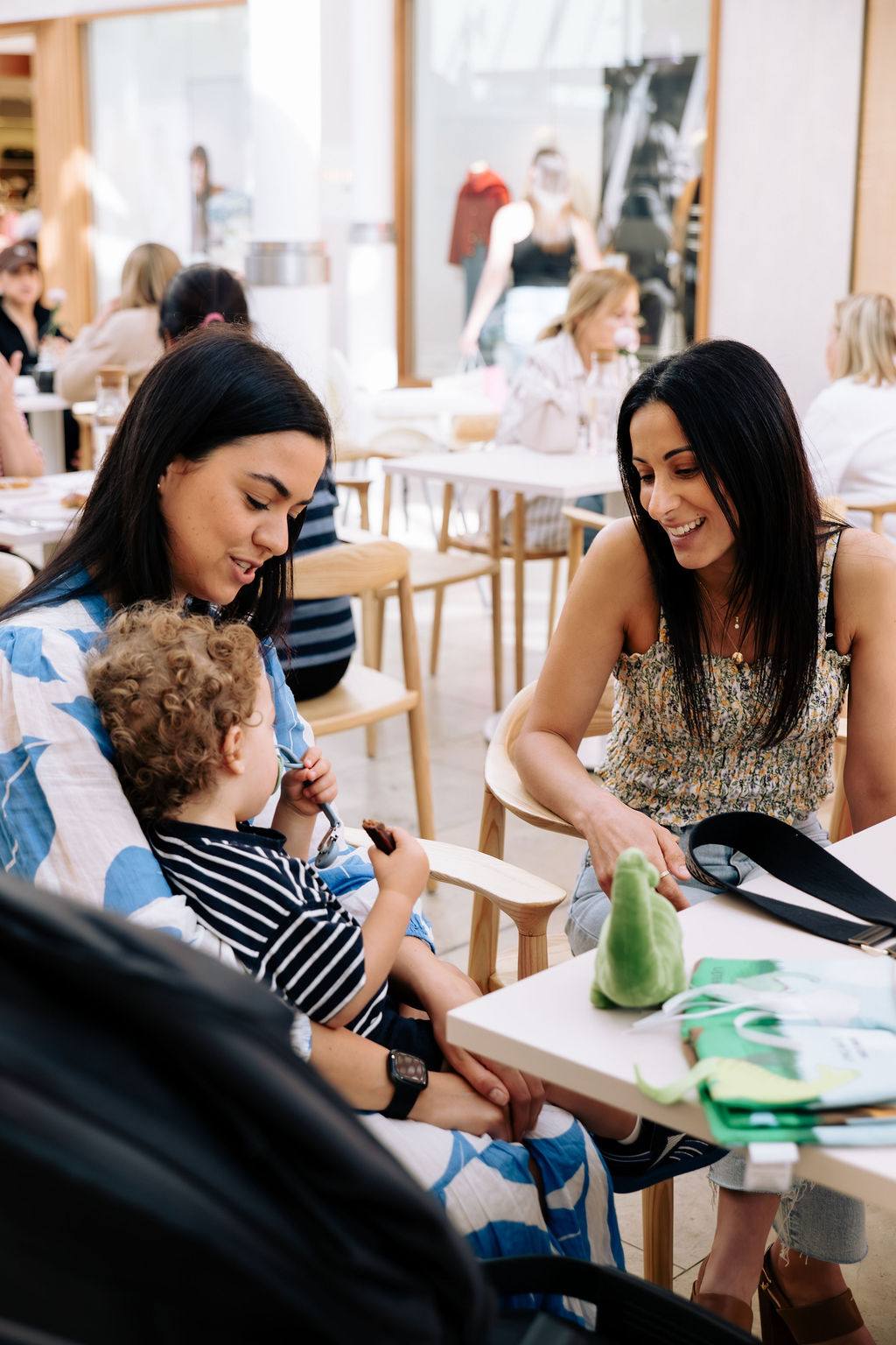 A mum with her toddler on her lap at an Open Coffee, another woman smiling at the baby