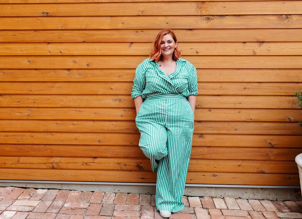 Leaning against a timber wall, smiling, hands in pockets