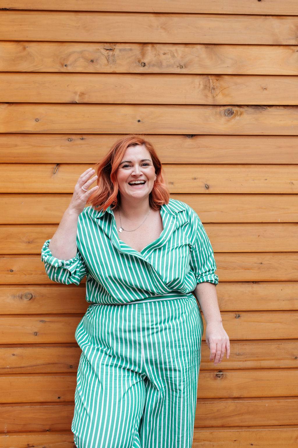 Woman in a green striped outfit laughing in front of a timber wall